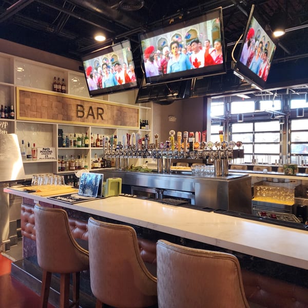 A well-stocked bar at Garnish Restaurants with multiple beer taps, liquor bottles, and TVs showing Indian content.