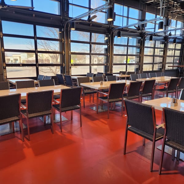 Garnish Restaurants' dining area with red floors, light tables, dark chairs, and large glass garage doors.