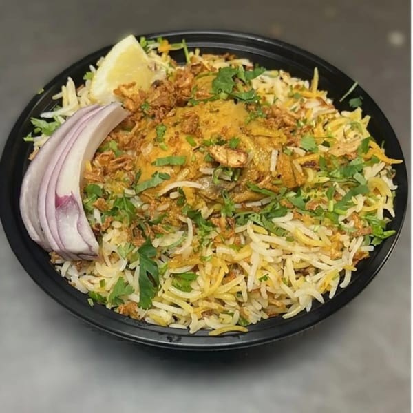 Indian chicken biryani with rice, fried onions, cilantro, red onion, and a lemon wedge.