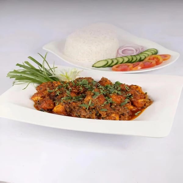 Indian chicken curry with cilantro, served with white rice, sliced cucumbers, tomatoes, and onions.