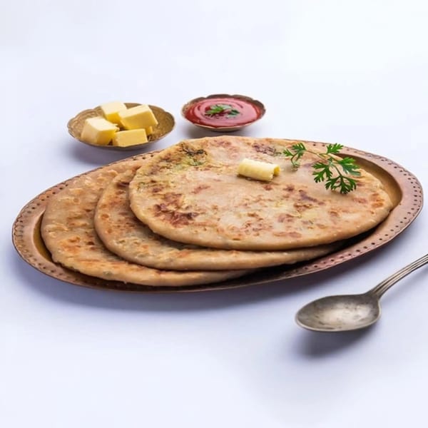 Three Indian parathas on a bronze plate with butter, ketchup, and a spoon.
