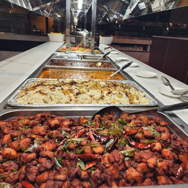 A buffet line at Garnish Restaurants with Indian dishes including chicken 65, biryani, and curries.