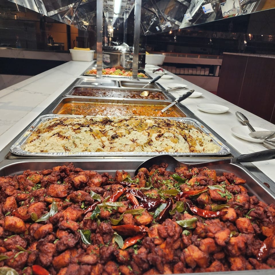 A buffet line at Garnish Restaurants with Indian dishes including chicken 65, biryani, and curries.