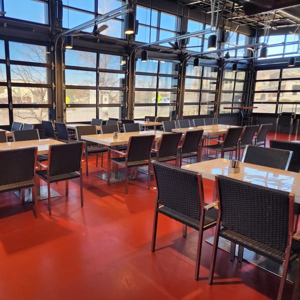 Garnish Restaurants' dining area with red floors, light wooden tables, and dark chairs, bathed in natural light.