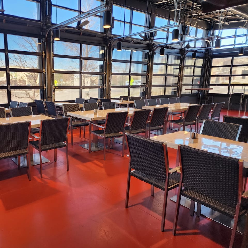 Garnish Restaurants' dining area with red floors, light wooden tables, and dark chairs, bathed in natural light.
