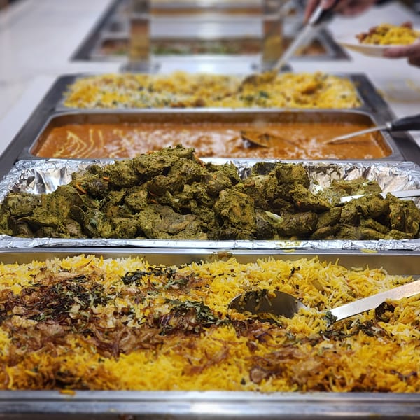 A buffet line with trays of Indian food, including biryani, green curry, and orange curry.