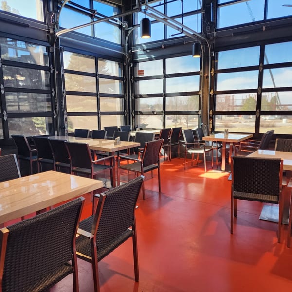 Bright, empty Garnish Restaurants dining room with red floor, light wood tables, and large glass garage doors.