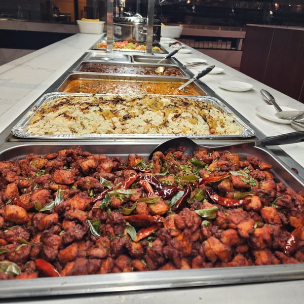 A buffet line with trays of Indian food, including chicken 65, biryani, and curries.