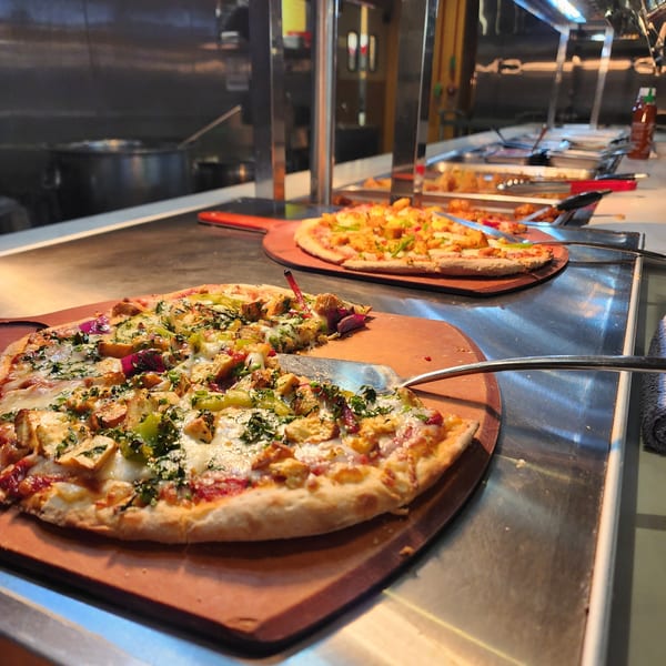 Two Indian-style pizzas with paneer and vegetables on wooden peels at a buffet line.