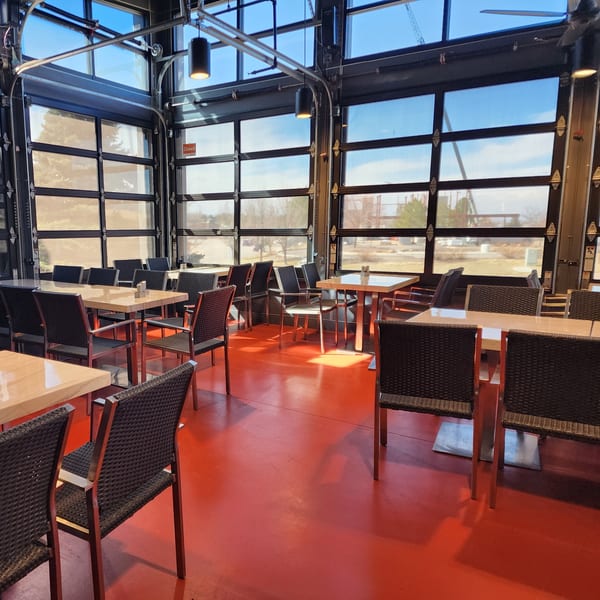 Garnish Restaurants' dining area with red floor, light wood tables, and large glass garage doors.
