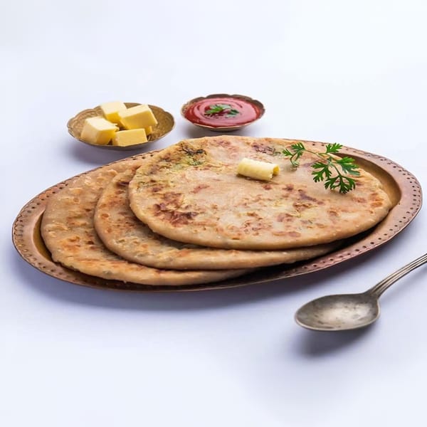 Three Indian parathas on a bronze plate, with butter, ketchup, and a spoon.