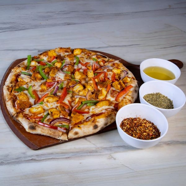 Indian-style pizza with chicken, bell peppers, and onions, served with olive oil and spices.