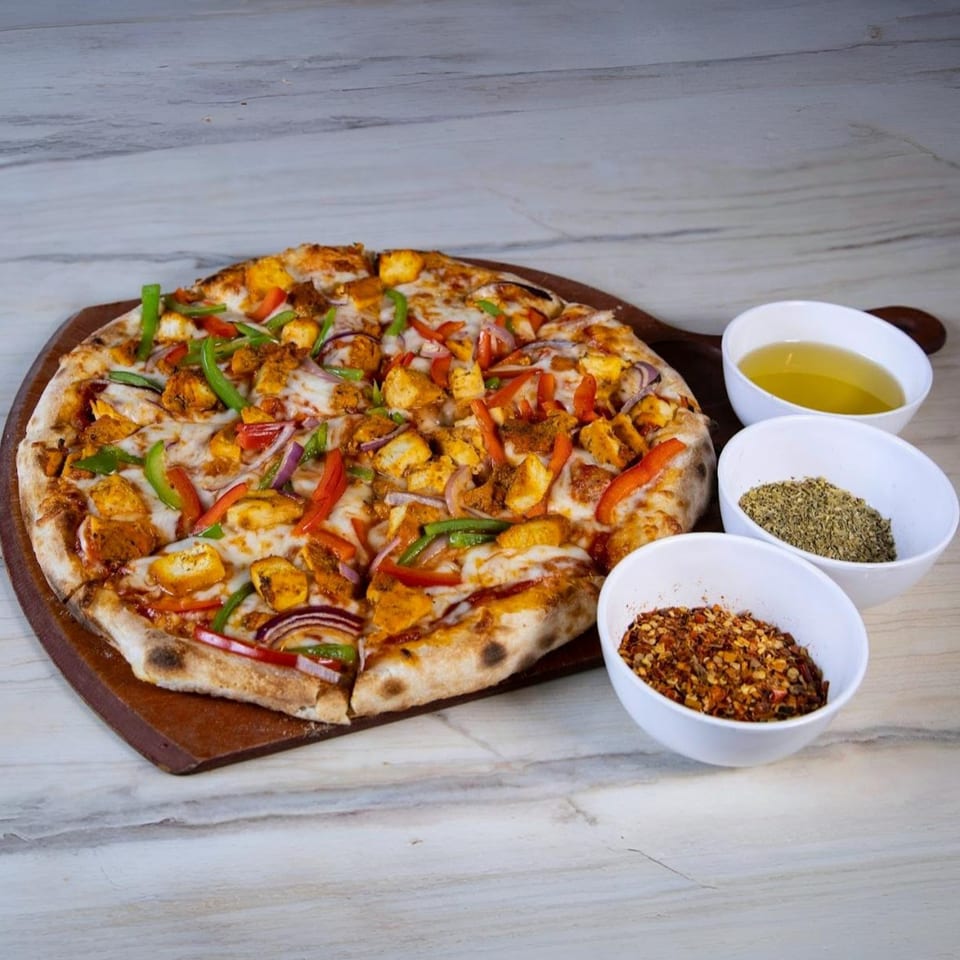 Indian-style pizza with chicken, bell peppers, and onions, served with olive oil and spices.