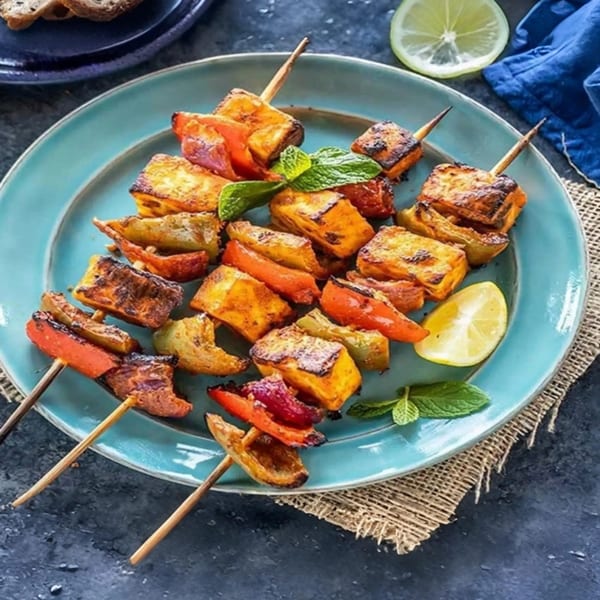 Indian paneer tikka skewers with bell peppers and mint on a blue plate.