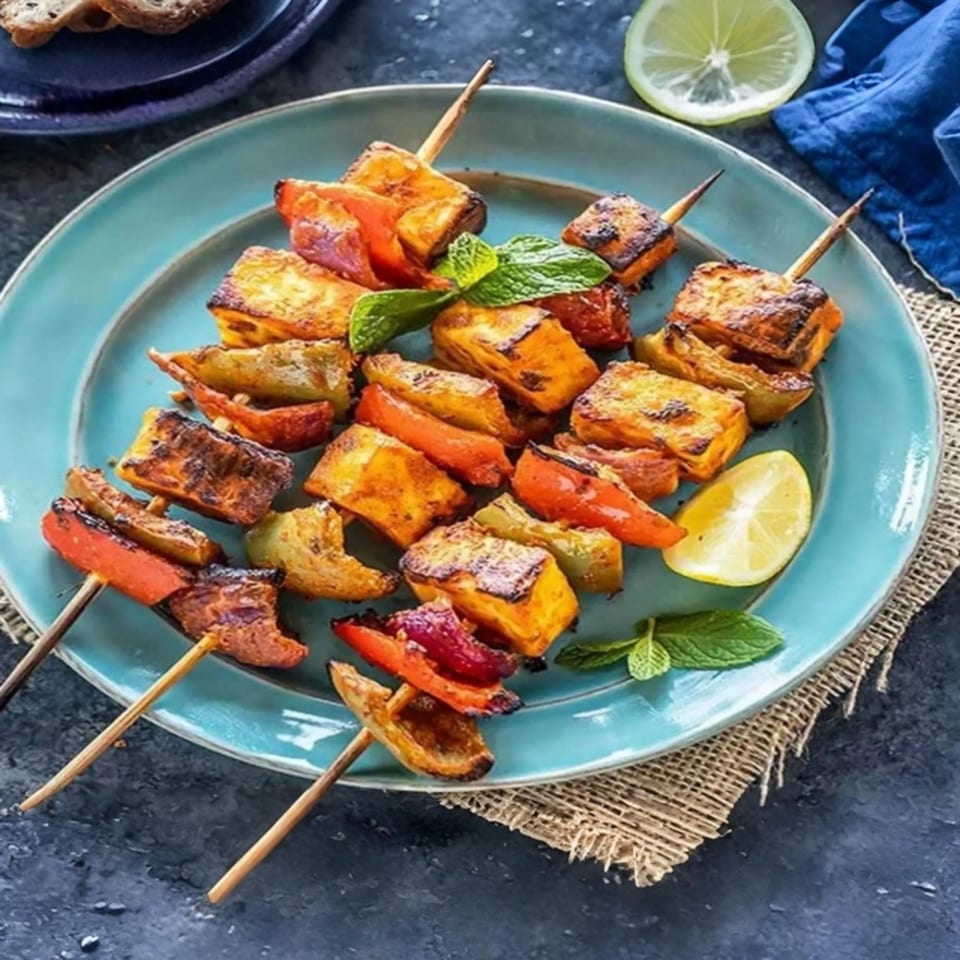 Indian paneer tikka skewers with bell peppers and mint on a blue plate.