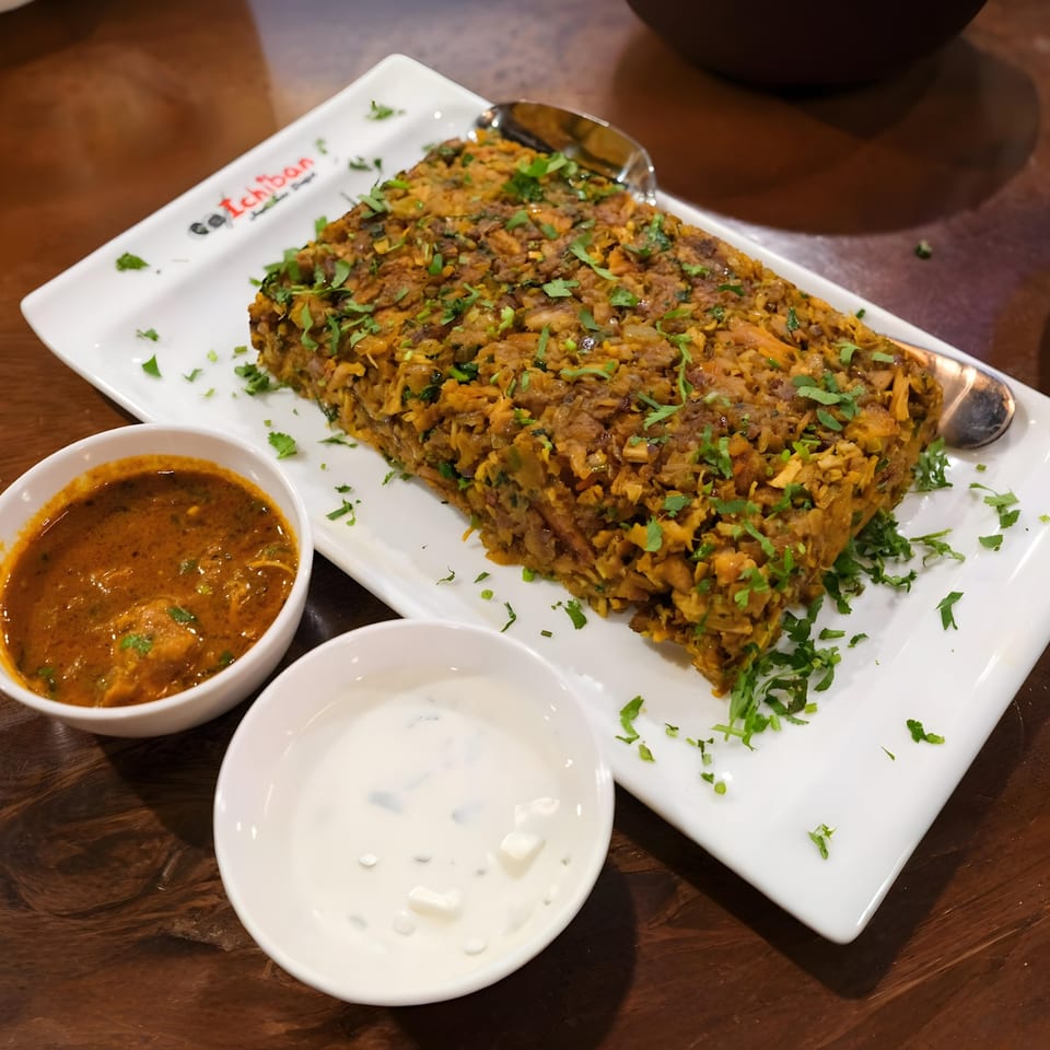 Indian biryani dish with cilantro, served with two side sauces on a white rectangular plate.