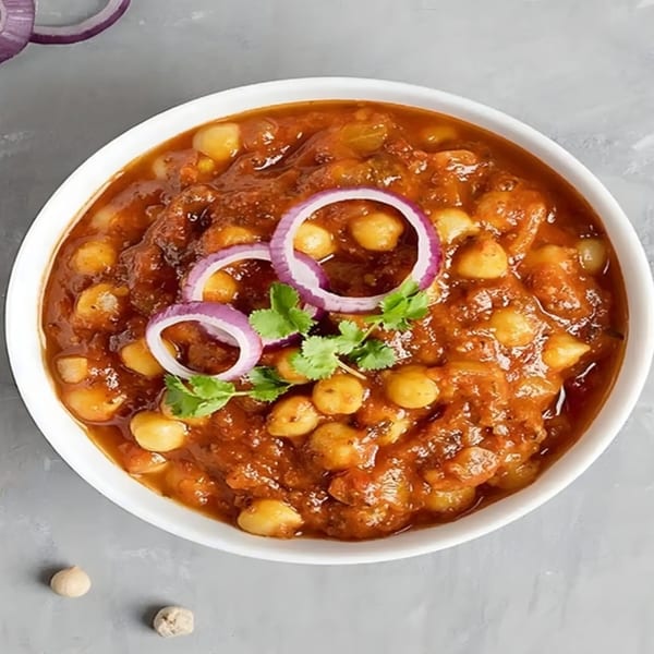 A white bowl filled with Indian chana masala, garnished with red onion rings and fresh cilantro.