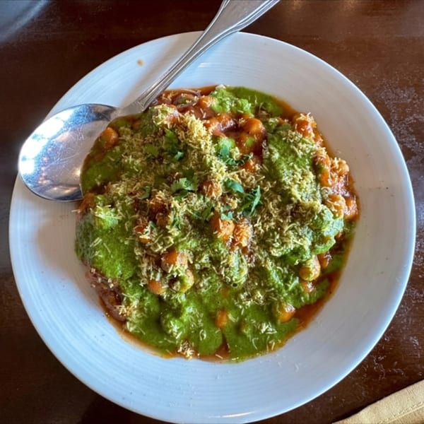 Indian chaat dish with green chutney, chickpeas, and crispy sev on a white plate with a spoon.