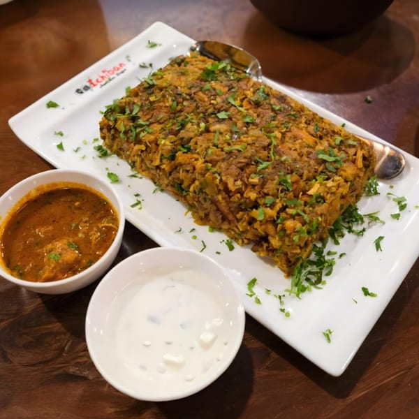 Indian biryani with cilantro, served with two dipping sauces on a white rectangular plate.