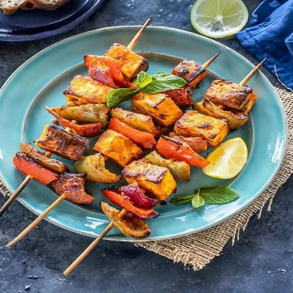 Indian paneer tikka skewers with bell peppers and onions, garnished with mint and lime on a blue plate.