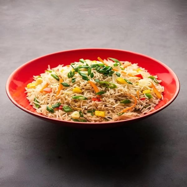 A vibrant red bowl filled with Indian vegetable fried rice, garnished with colorful vegetables.